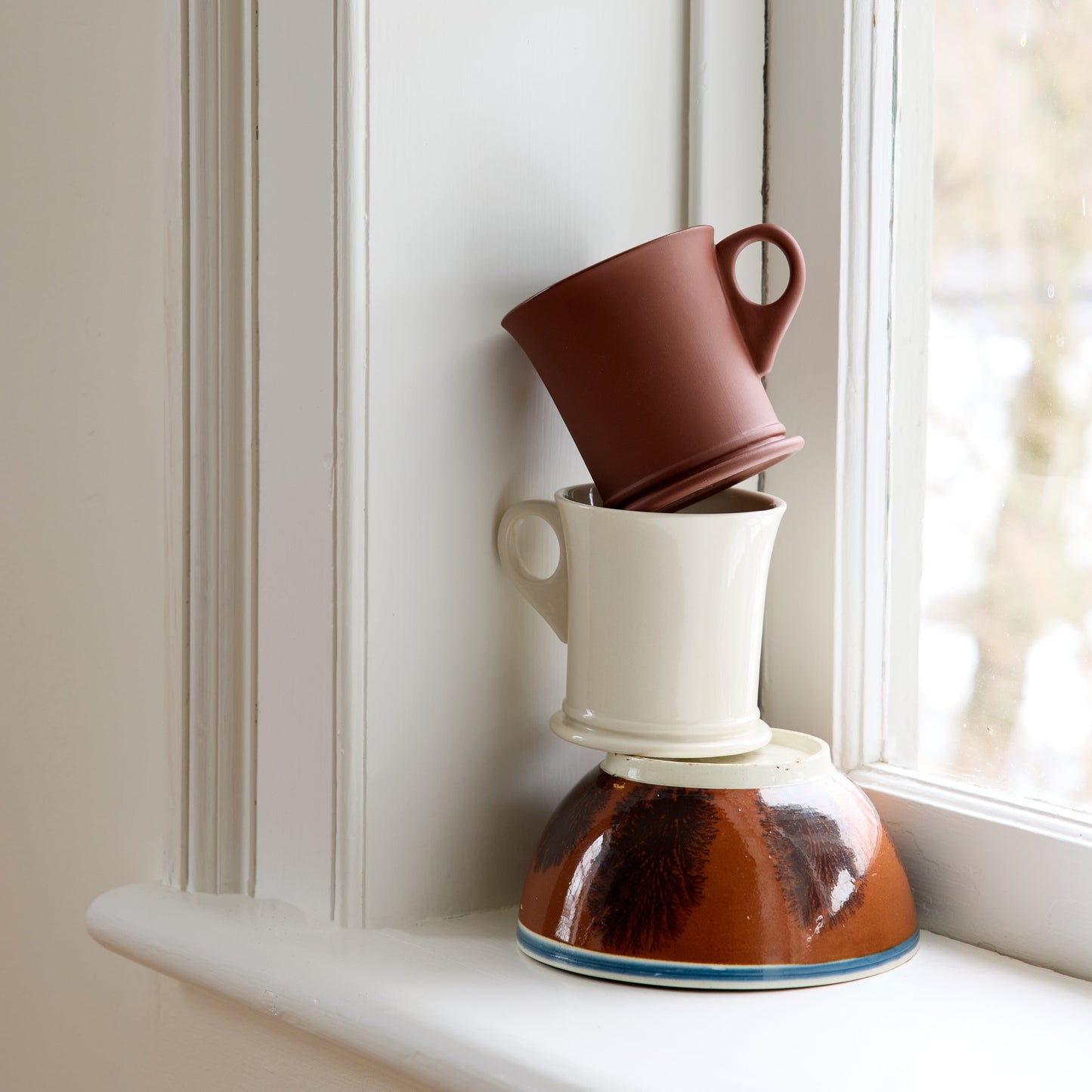 Stack of ceramic mugs on a windowsill with natural light