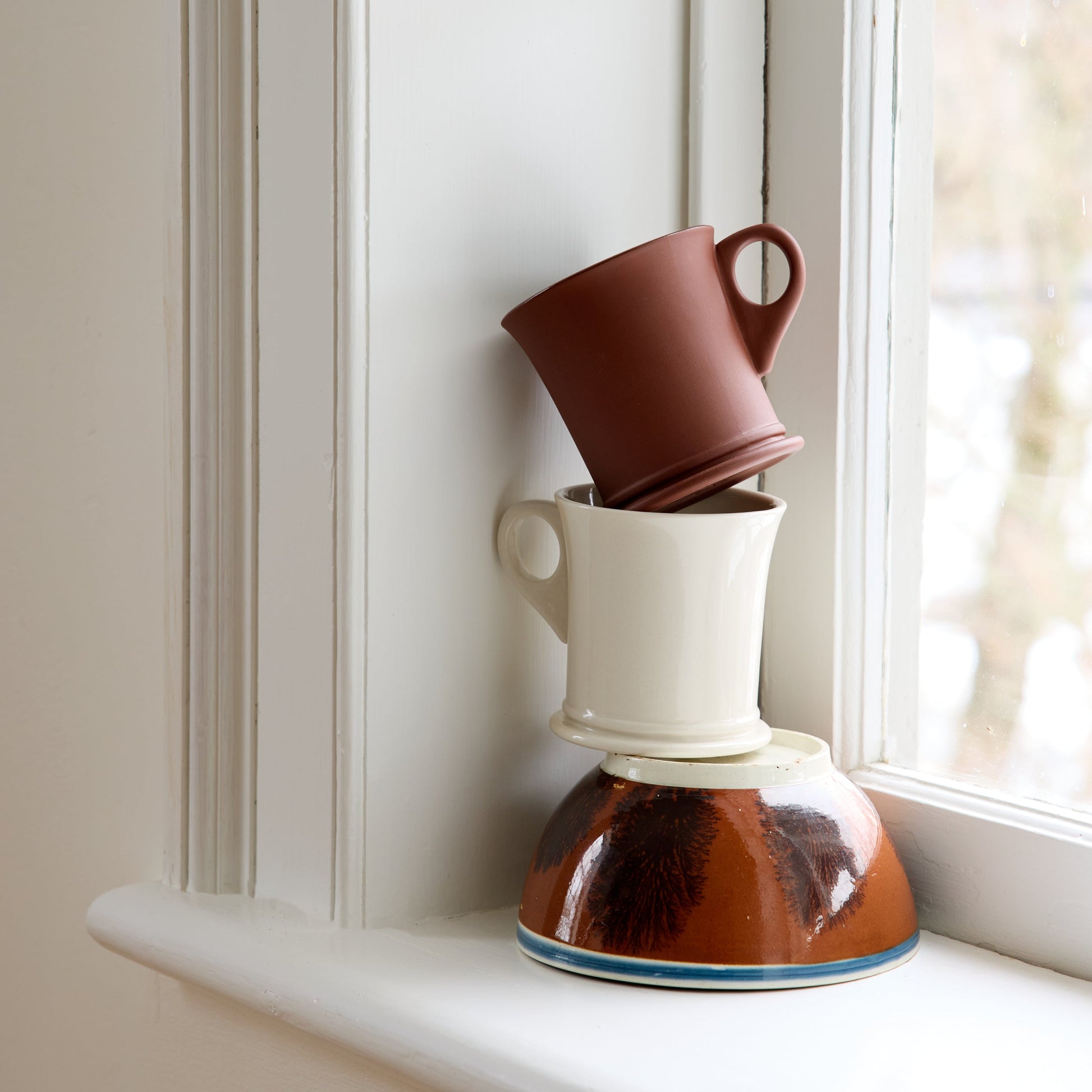 Stack of ceramic mugs on a windowsill with natural light