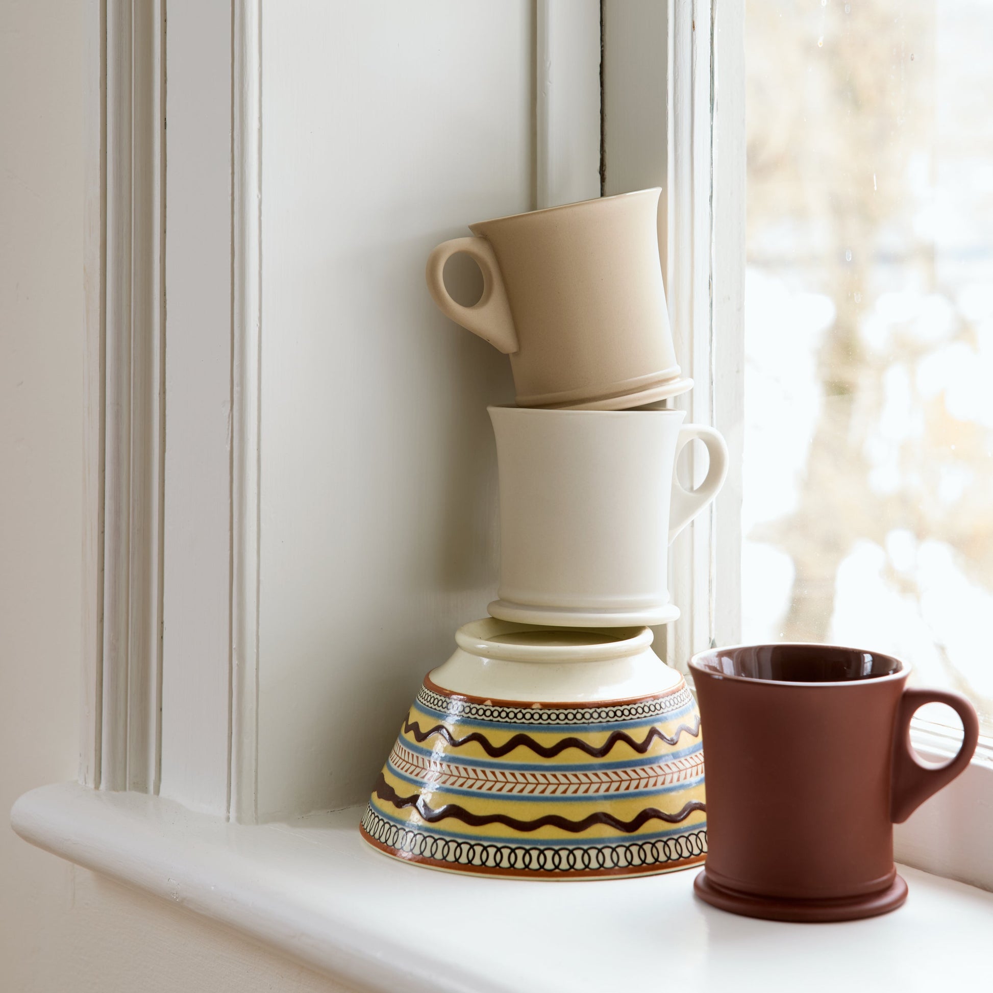 Stack of ceramic mugs on a windowsill with natural light