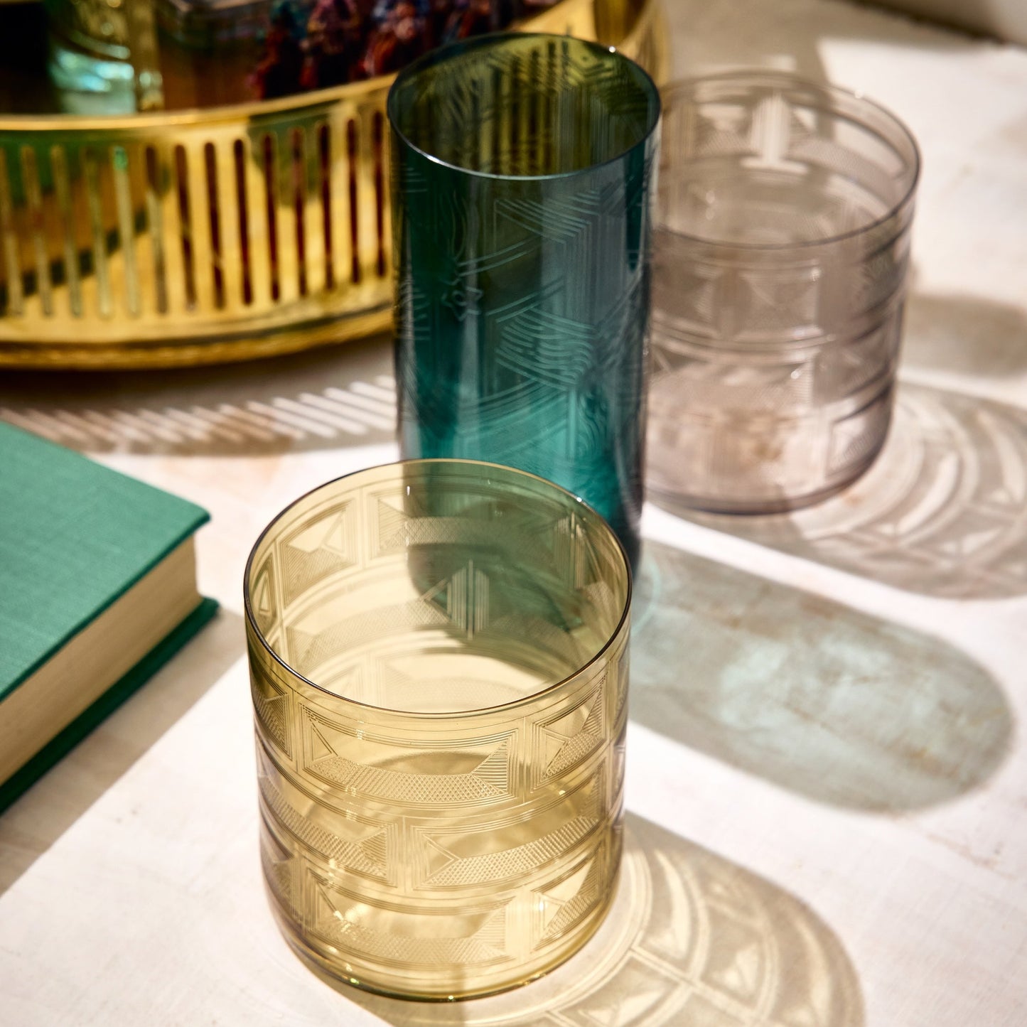 Two glass tumblers, one green and one amber, on a light surface with a blurred background.