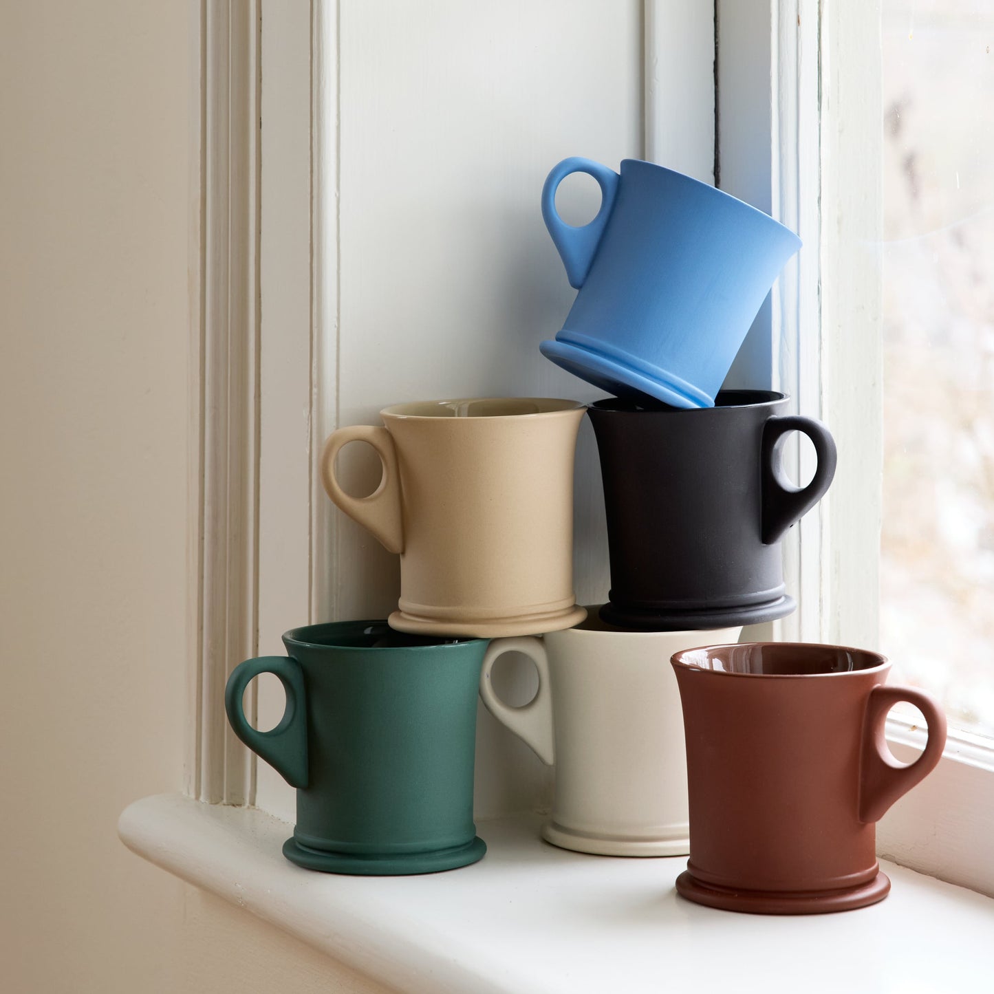 Set of colorful mugs stacked on a windowsill